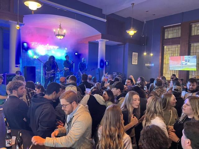 A packed room watching Random Riot play, crowd shoulder to shoulder in front of the stage