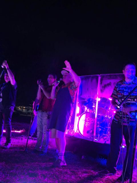People dancing in front of the stage under magenta light at an outdoor night show