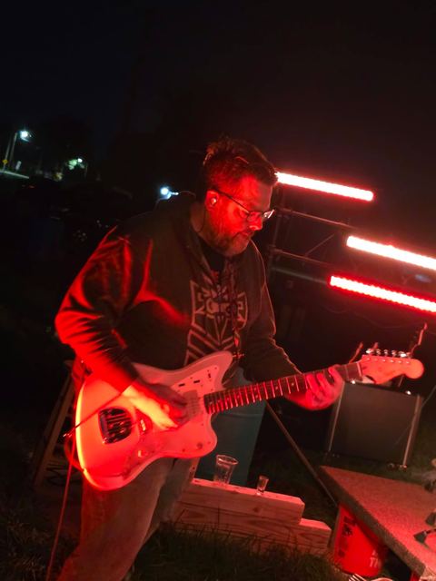 Guitarist mid-song beside red LED bars