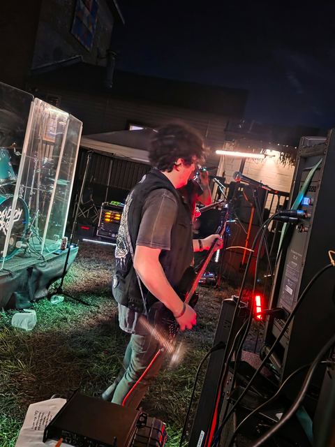Guitarist beside the drummer's shield, lit teal