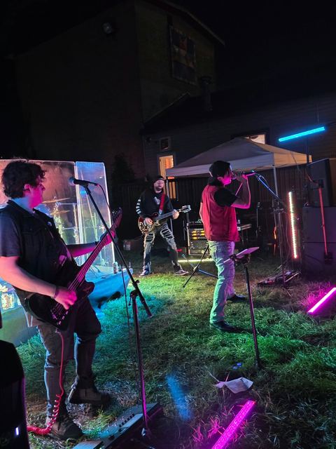 Random Riot playing an outdoor night show, the full band lit by LED tubes on a grass stage