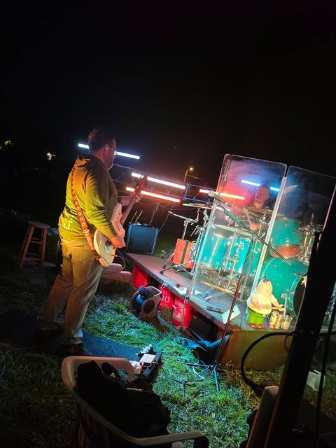 The band on an outdoor stage, warm light picking out the guitarist