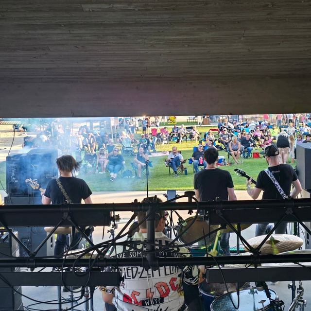 A large crowd spread across the grass at an outdoor park show, seen from the stage